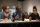 Three people sit at a table covered with water bottles, coffee cups and pads of paper.
